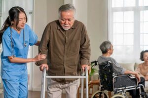 An older adult sits with a caregiver at a dining table, both smiling and engaged in friendly conversation.