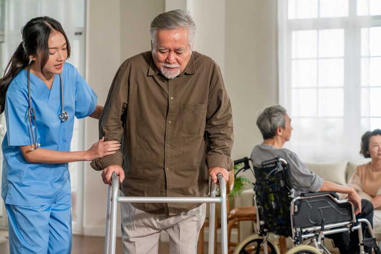 An older adult sits with a caregiver at a dining table, both smiling and engaged in friendly conversation.