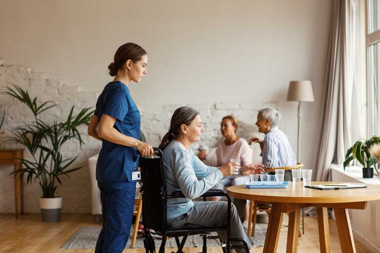 Senior residents using a tablet together in a cozy living room setting with staff nearby for assistance.